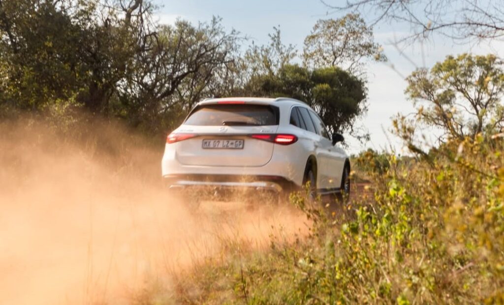 Rear view of a white Mercedes-Benz GLC Coupe kicking up a thick dust cloud on a gravel road, showcasing its dynamic handling outside the city