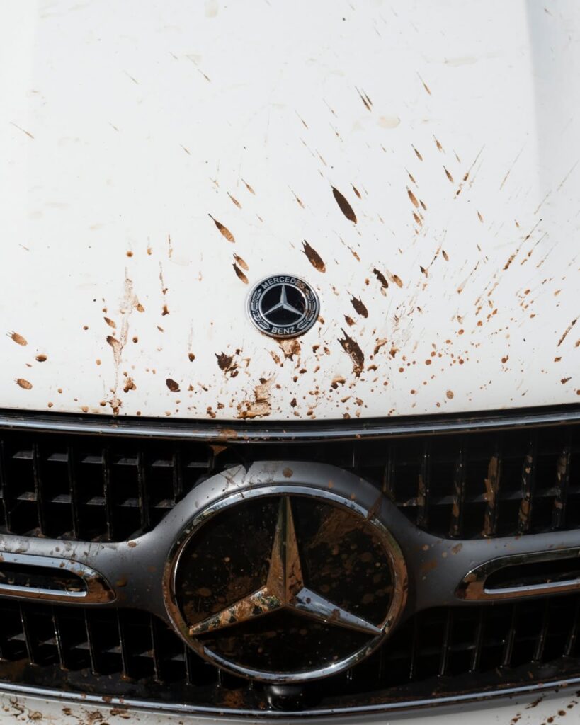Close-up of a mud-splattered Mercedes-Benz badge and grille on the GLC Coupe, proving it is highly capable of rugged gravel travel