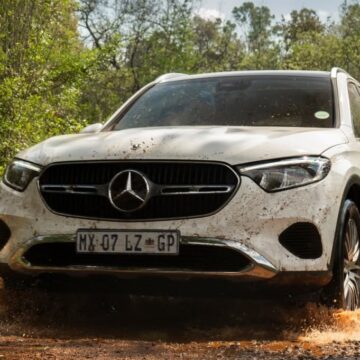 Action shot of a white Mercedes-Benz GLC Coupe splashing aggressively through a deep mud puddle, demonstrating its impressive 4x4 performance on dirt tracks
