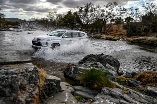 A white Mitsubishi Pajero Sport splashing through a river, demonstrating its readiness to tackle deep water crossings with ease